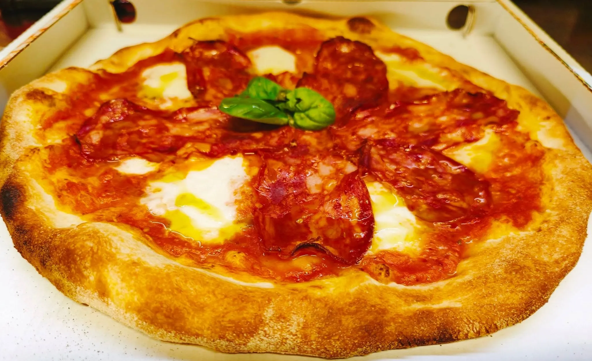 Pizza diavola con bufala e basilico appena uscita dal forno, nel cartone da asporto