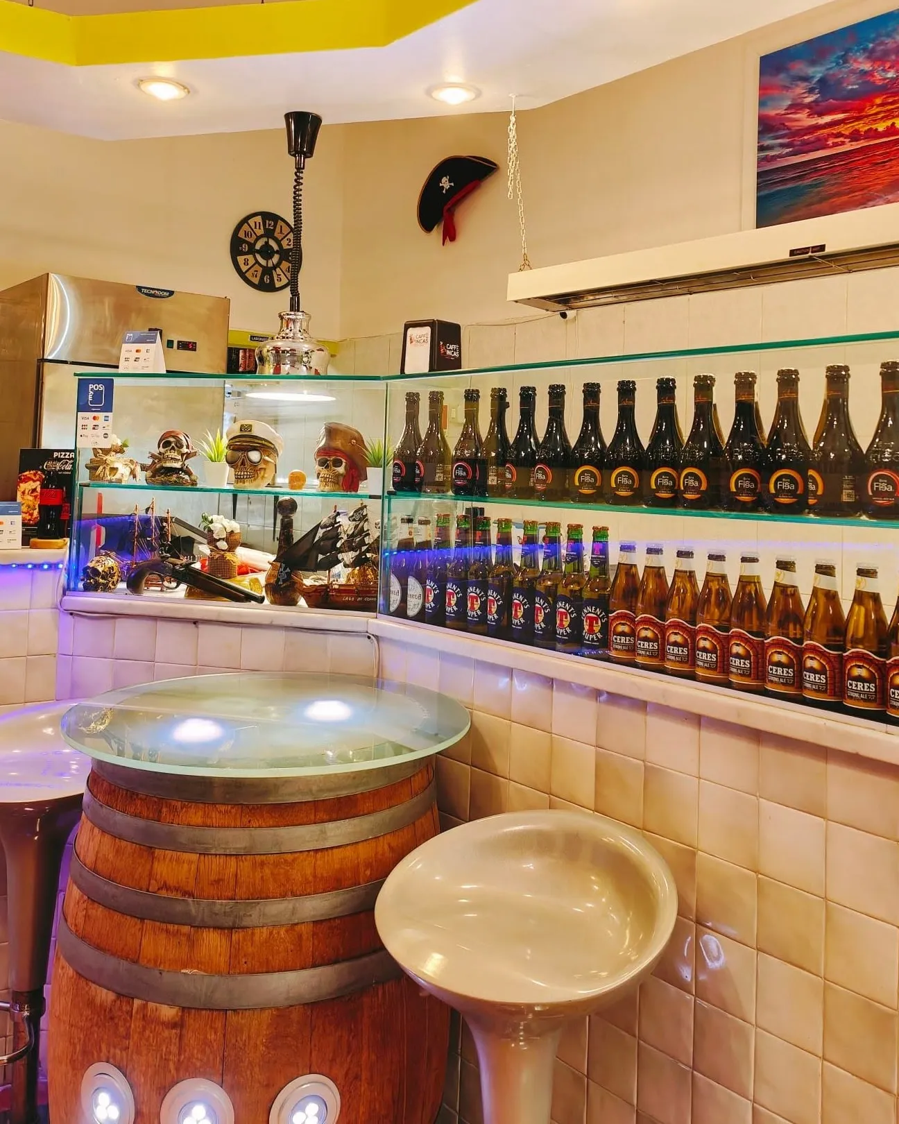 L'interno della pizzeria: il bancone, le birre in fila sulla mensola e il tavolino ricavato da una botte