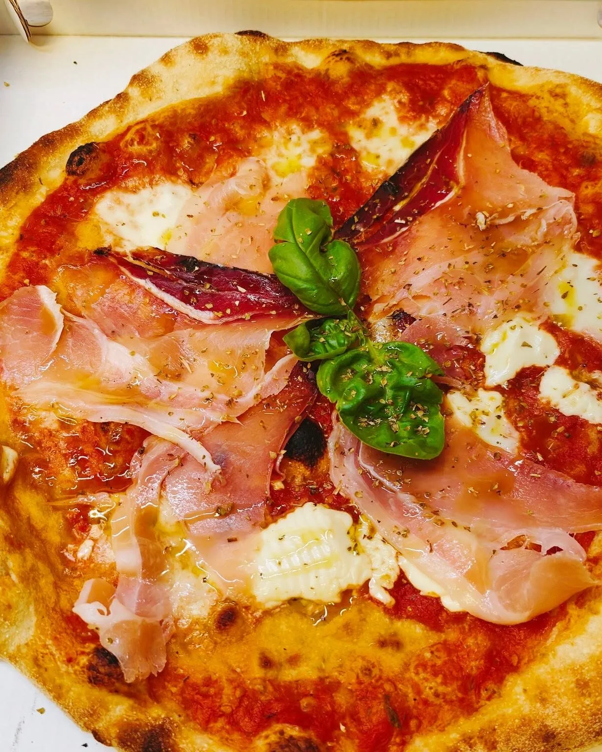 Pizza con prosciutto crudo, bufala e basilico nel cartone, vista dall’alto